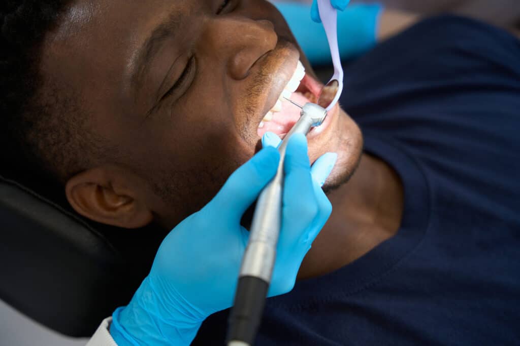 Dentist using a mirror and dental drill on patient